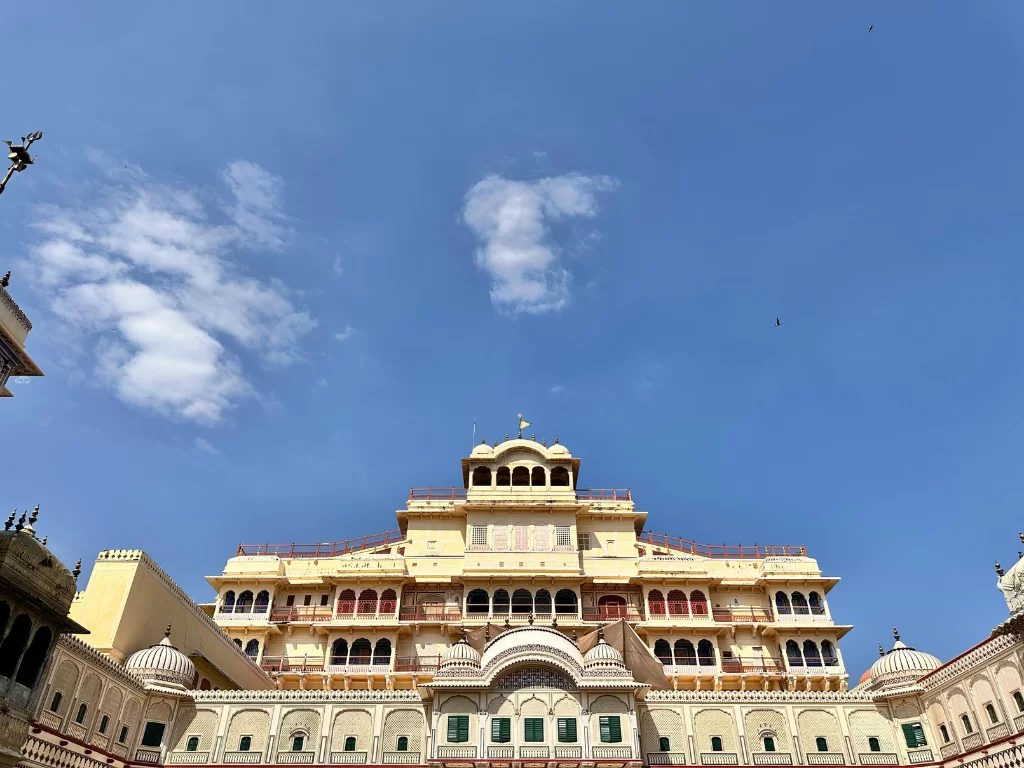 Towering yellow City Palace Jaipur Rajasthan grand facade with red arches green doors intricate balconies domes under partly cloudy blue sky classic heritage architecture, perfect Rajasthan tour package