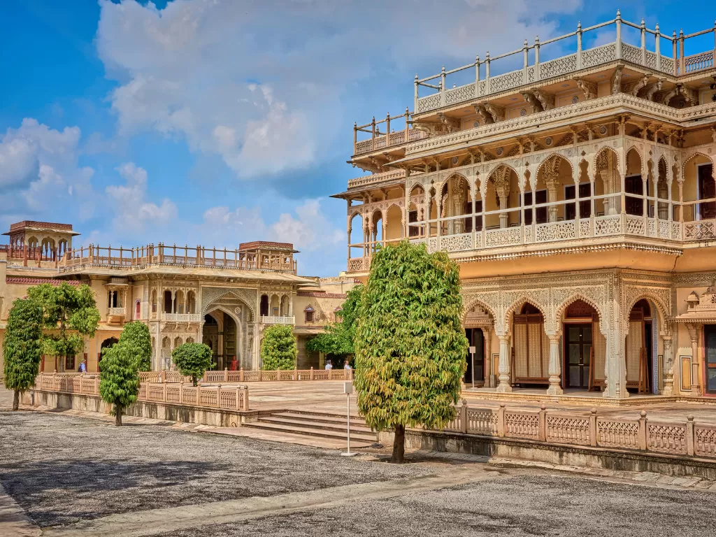Elegant sandstone Mubarak Mahal courtyard at City Palace Jaipur Rajasthan with trees ornate railings arched balconies under partly cloudy blue sky serene palace complex view, perfect Rajasthan tour package