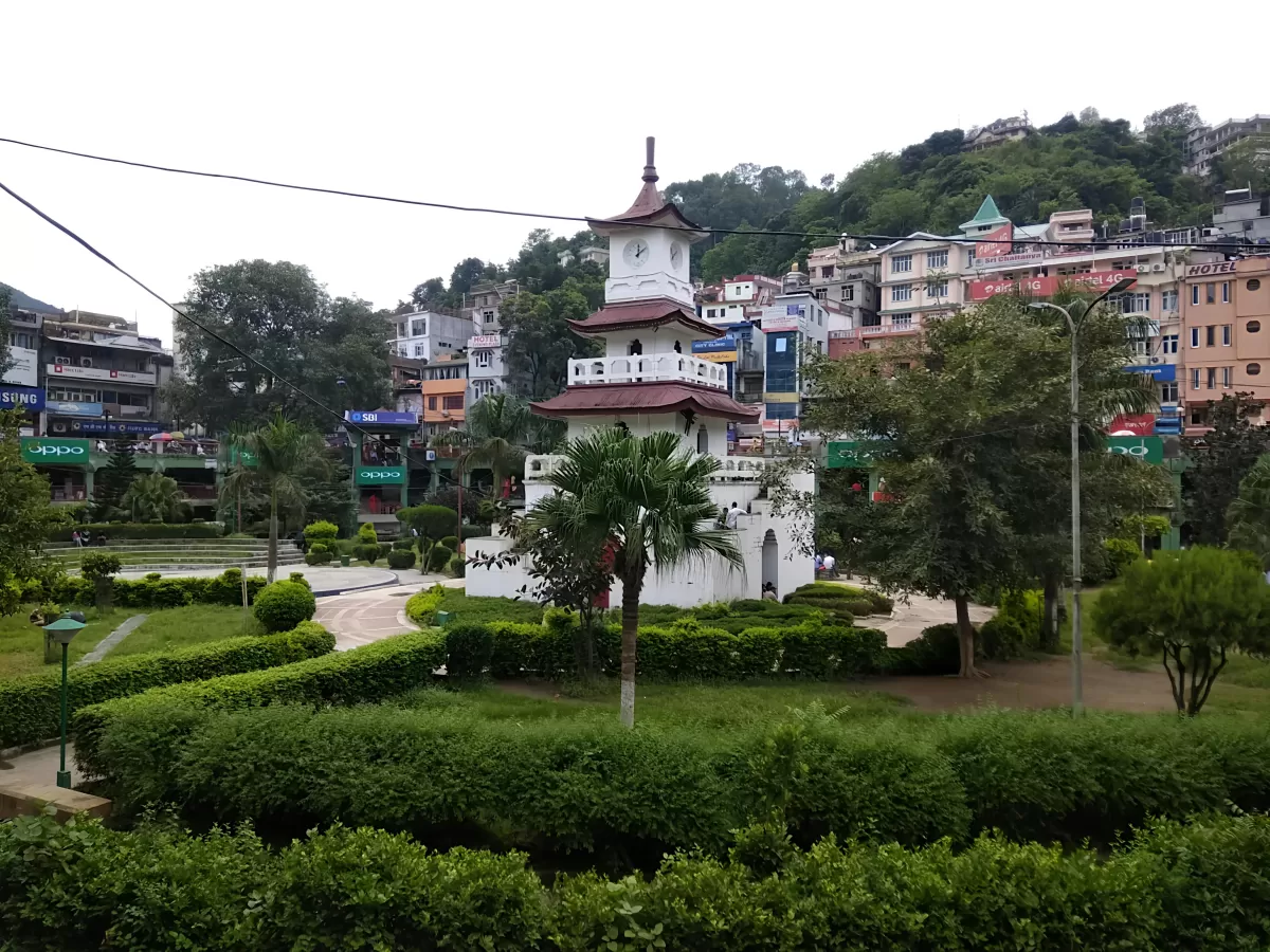 Clock Tower at Mandi Himachal Pradesh during misty afternoon, featuring white pagoda tower with palms amid town buildings and hills, perfect heritage experience Himachal Pradesh tour package.