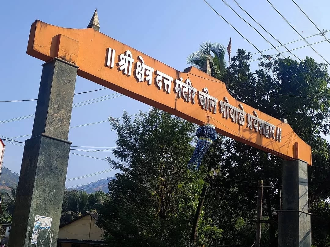 Entrance arch of Datta Mandir in Maharashtra, featuring Marathi signage and surrounded by trees and local surroundings, a spiritual site included in Maharashtra tour packages.