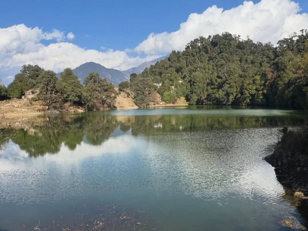 Deoria Tal in Uttarakhand reflecting surrounding forested hills and distant Himalayan peaks, a serene trekking destination included in Uttarakhand tour packages