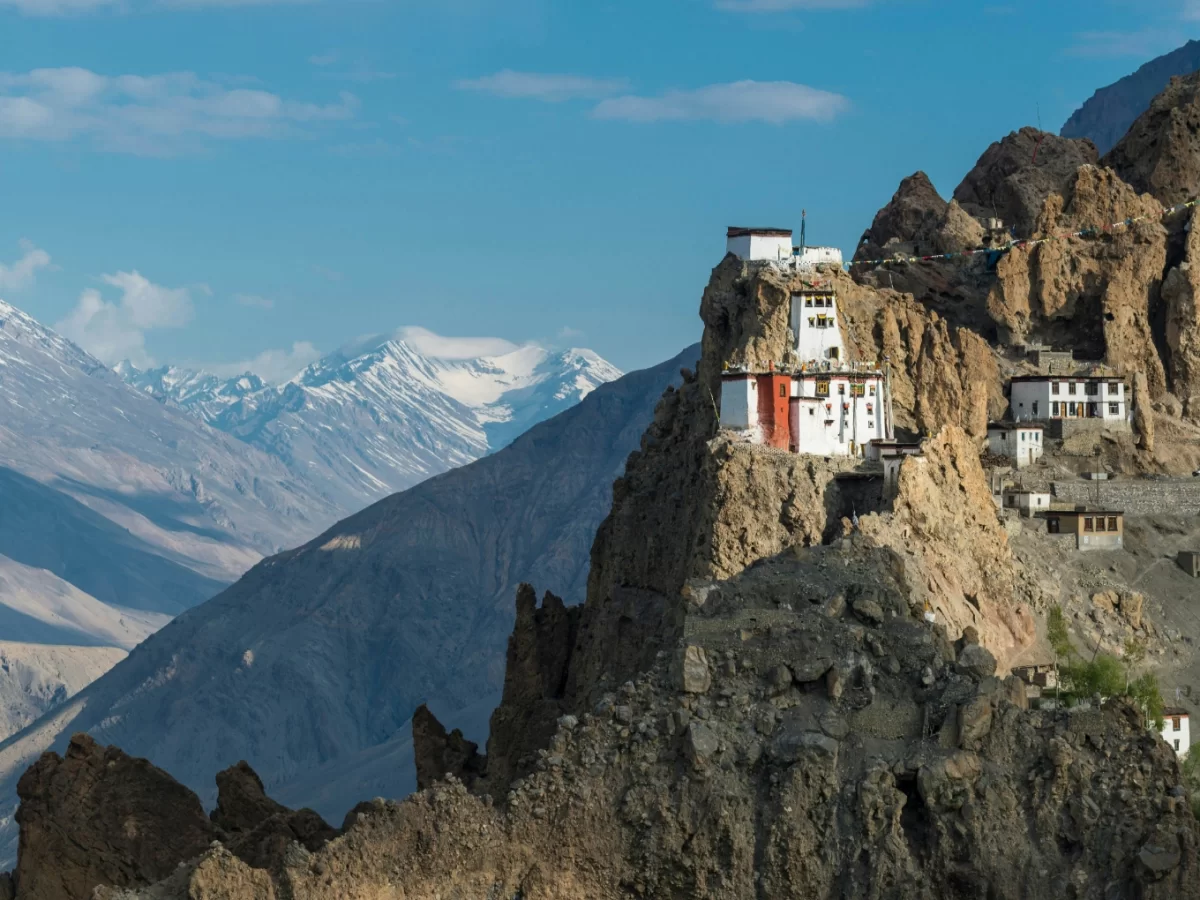 Dhanankar Monastery Kaza Spiti winter cliffside, featuring tiered white gompa red accents perched rocky outcrop snowy Himalayan ranges blue skies, perfect Himachal Pradesh tour packages.