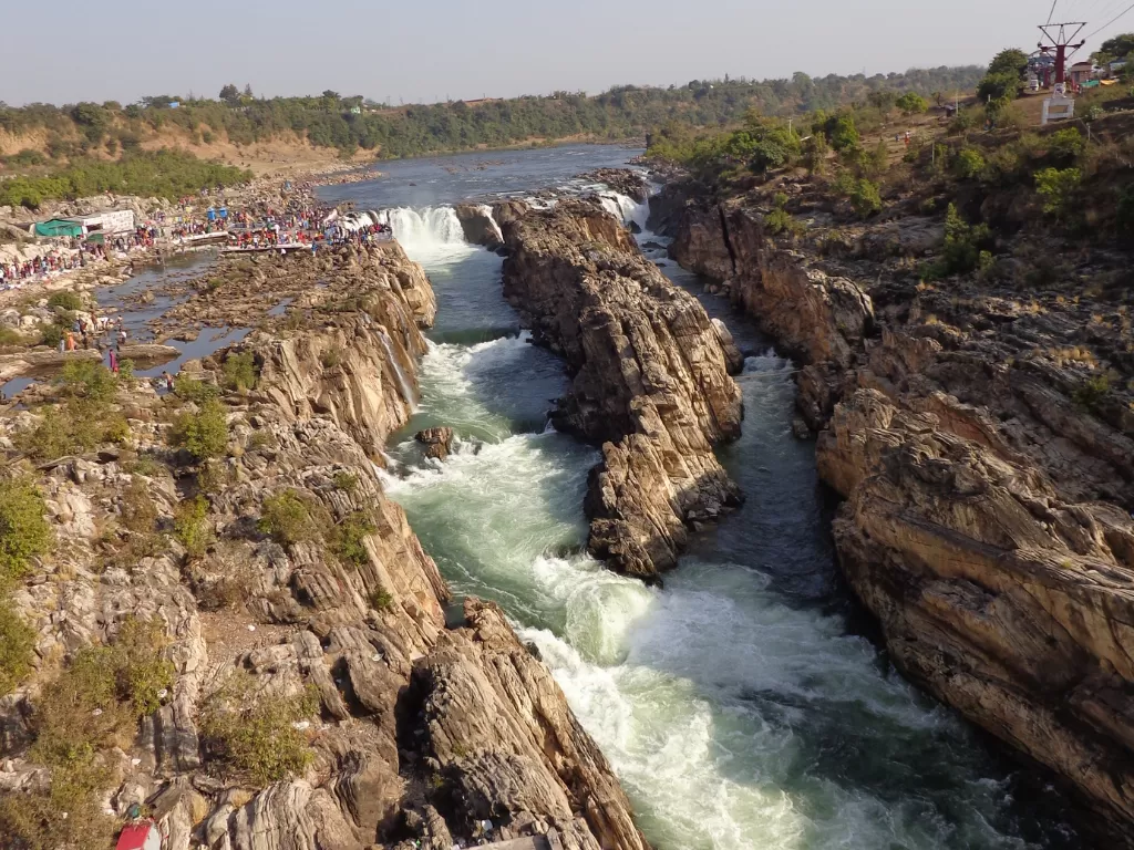 Dhuandhar Falls at Bhedaghat Jabalpur during clear afternoon, featuring roaring Narmada cascades through marble gorges and viewing platforms, perfect adventure experience in Madhya Pradesh tour package.
