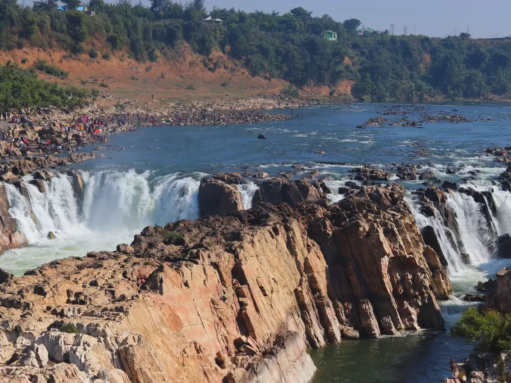 Dhuandhar Falls at Bhedaghat Jabalpur during golden afternoon, featuring cascading Narmada waters through marble gorges and tourist crowds, perfect adventure experience in Madhya Pradesh tour package.