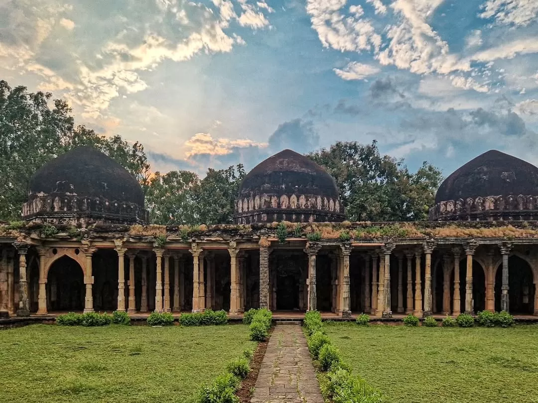 Dilawar Khan’s Mosque in Mandu, Madhya Pradesh, featuring three dark domes and a long arched colonnade courtyard under a dramatic evening sky, a historic highlight of Madhya Pradesh tour packages