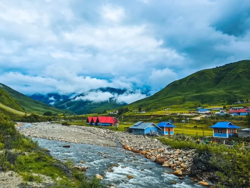 Dorjeeling Village scenic mountain settlement with colorful houses and flowing river amidst lush green hills in Arunachal Pradesh Package.