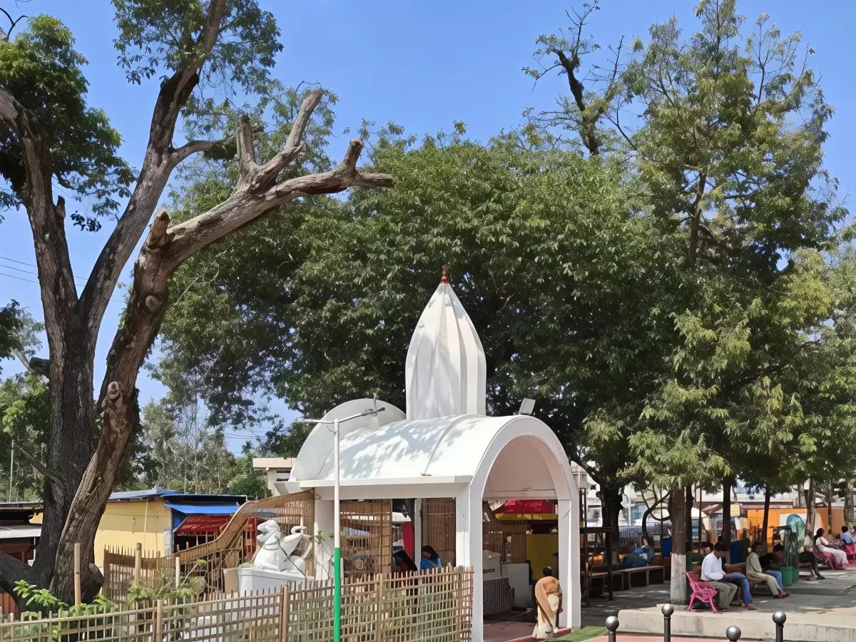 Small shrine at Doul Govinda Temple campus in North Guwahati during sunny day, featuring white pavilion, trees and seating area, perfect spiritual experience Assam tour package.