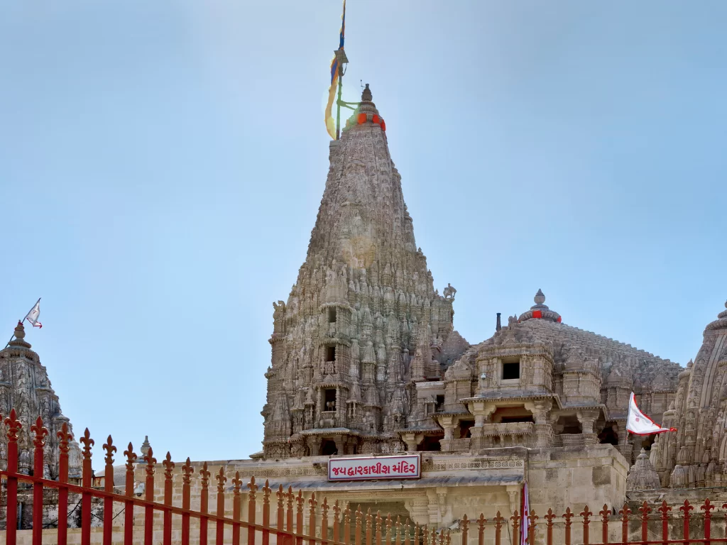 Dwarkadhish Temple in Dwarka during clear day, featuring towering multi-tiered shikhara with flags and red fence, perfect pilgrimage experience with Gujarat tour packages.