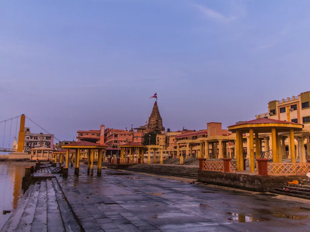 Dwarkadhish Temple at Gomti Ghat during sunset in Dwarka, featuring towering shikhara with flag, yellow pavilions over river steps, perfect pilgrimage experience with Gujarat tour packages.