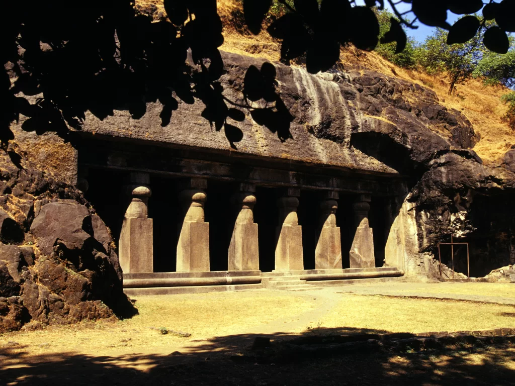 Elephanta Caves Mumbai shadowy rock-cut facade pillars lush greenery basalt cliff, UNESCO Shaiva temple shadows Trimurti Shiva Gharapuri, perfect ancient cave heritage shadows package.