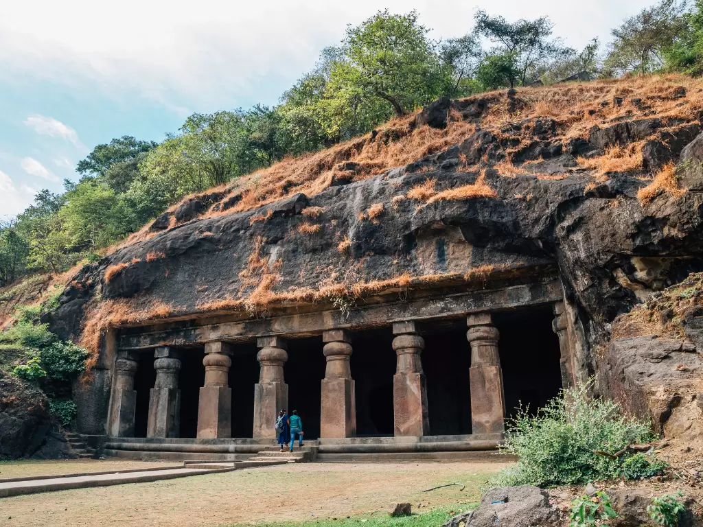 Elephanta Caves Mumbai tourists rock-cut facade pillars lush forested hillside blue sky, UNESCO Shaiva grand porch Shaivism sculptures Gharapuri, perfect ancient cave heritage adventure package.
