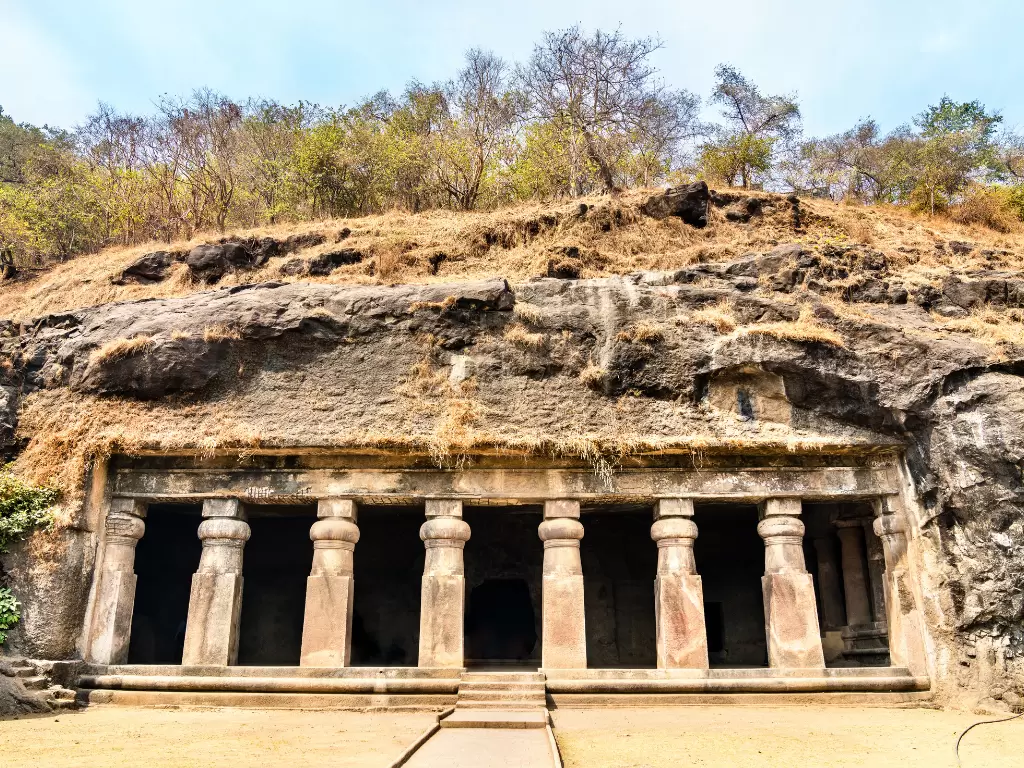 Elephanta Caves Mumbai iconic rock-cut facade pillars forested hillside blue skies, UNESCO Shaiva grand hall Shiva sculptures Gharapuri island, perfect Mumbai heritage cave exploration package.
