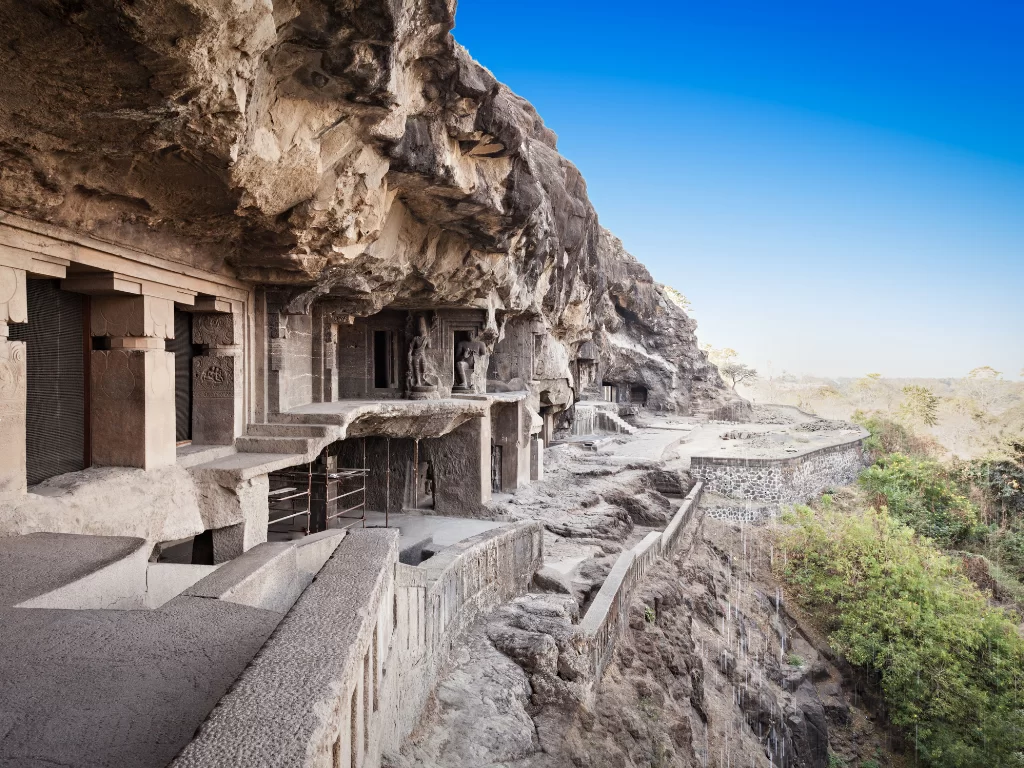 Jain caves series carved into cliffside at Ellora Caves during clear blue sky, featuring rock facades, wall, greenery, perfect UNESCO Aurangabad tour package. 