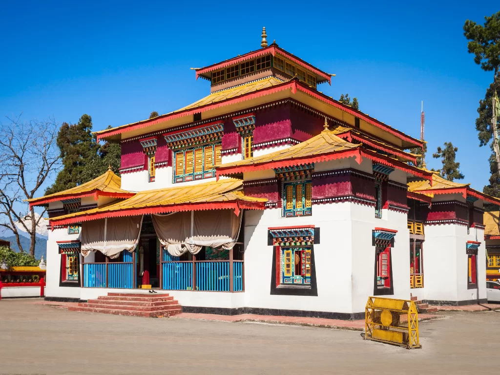Traditional Enchey Monastery in Gangtok with vibrant Sino-Tibetan architecture, multi-tiered pagoda-style roof and colorful carved windows under clear blue Himalayan sky Sikkim tour packages.