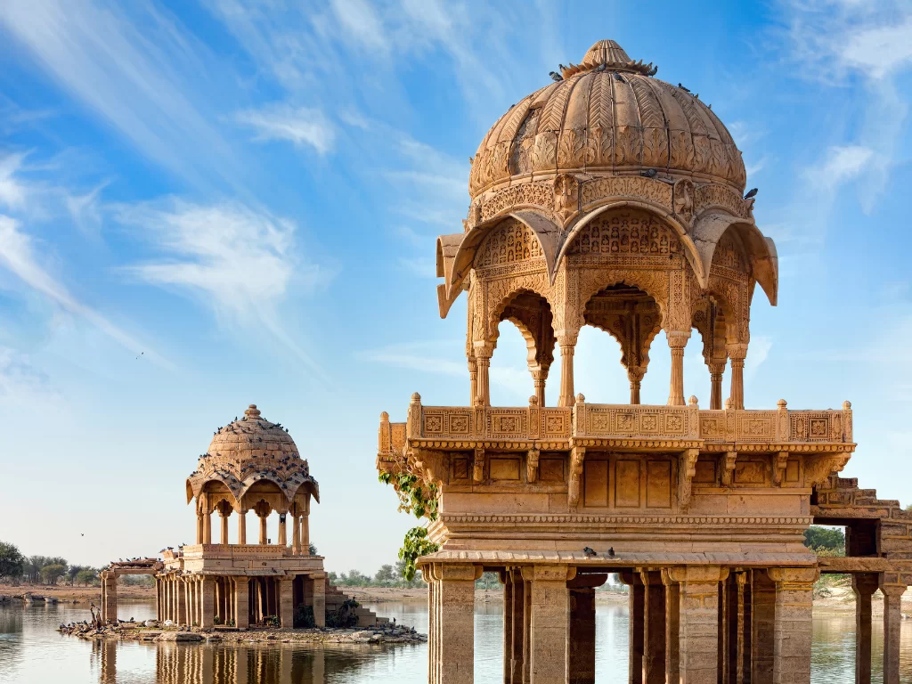 Gadisar Lake iconic sandstone pavilions & temples on water amid blue skies, perfect cultural heritage Jaisalmer Rajasthan tour packages.