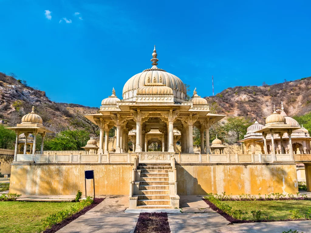 Gaitor Ki Chhatriyan Jaipur majestic cluster golden sandstone Rajput cenotaphs domed pavilions intricate carvings steps landscaped gardens Aravalli hills backdrop blue sky, royal memorial heritage complex tour package.