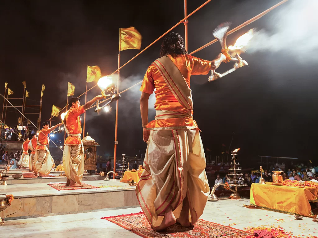 Ganga Aarti priests with flames at Varanasi during night, featuring flags lamps smoke rituals, perfect spiritual Uttar Pradesh tour package.