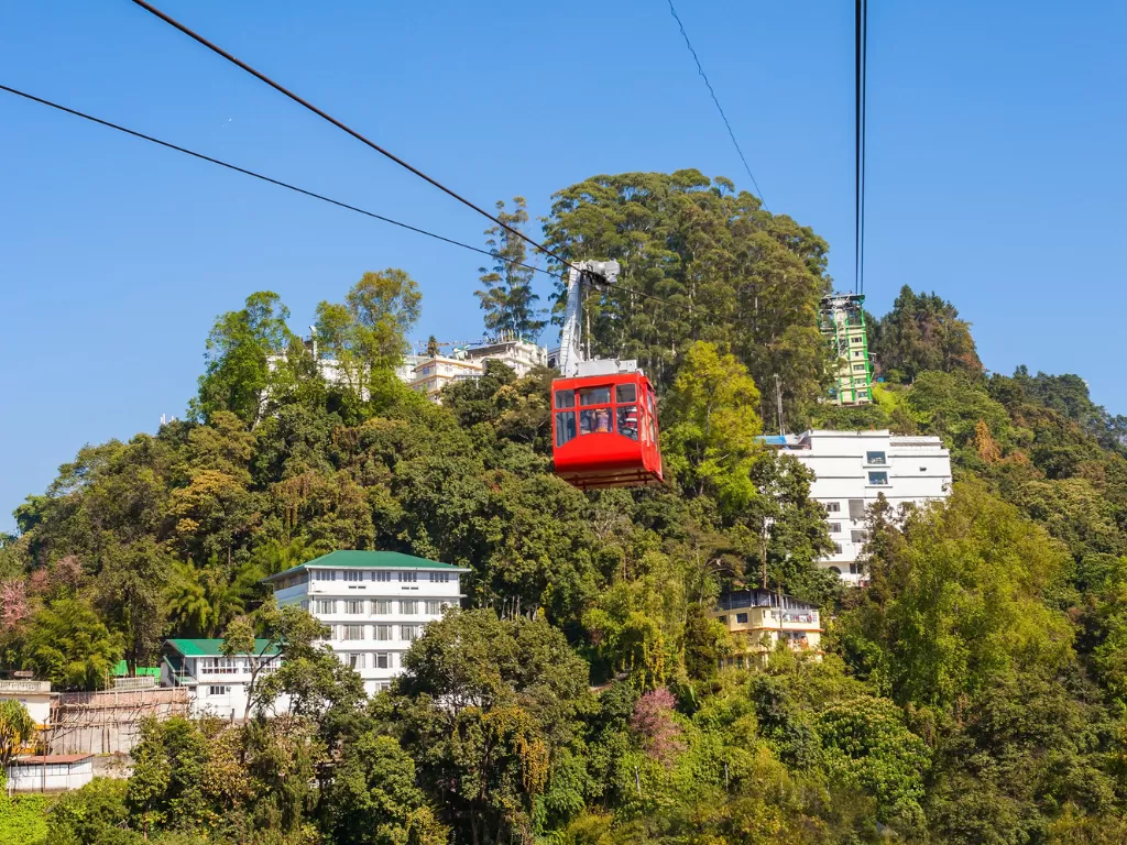 Gangtok Ropeway cable car gliding above forested hillside and town buildings during clear daylight, offering panoramic city and valley views, perfect family Sikkim tour package.