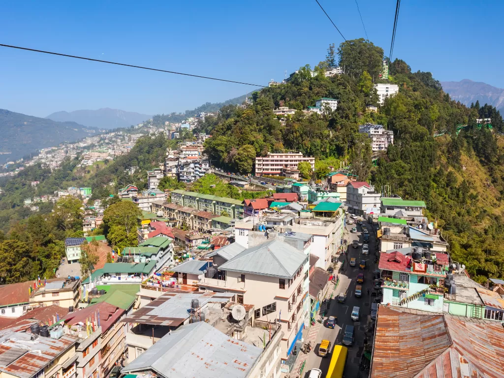 Gangtok cityscape from Gangtok Ropeway during clear daylight, featuring hillside buildings, busy main road and distant valleys, perfect cityscape Sikkim tour package.