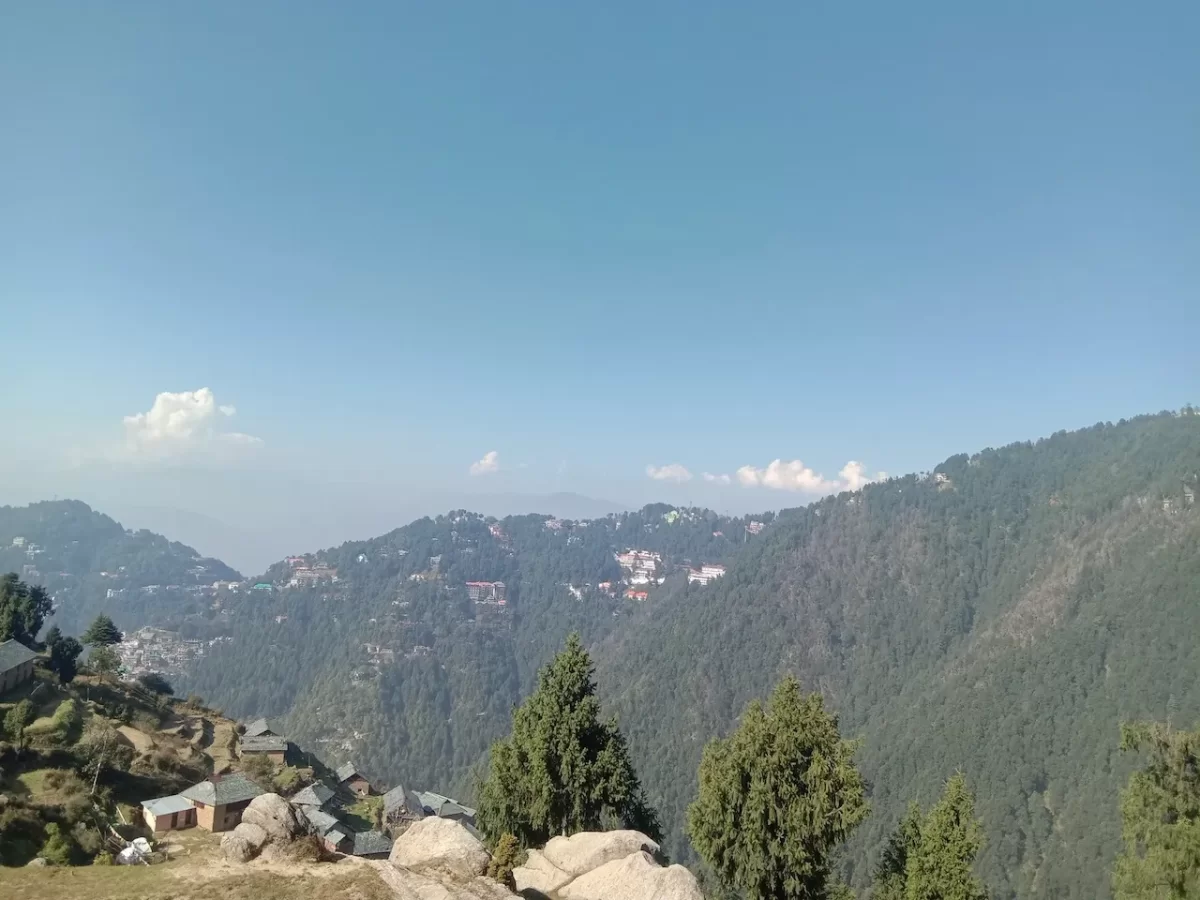 Panoramic view from Ganji Pahari at Dalhousie during clear sky, featuring pine trees, misty Dhauladhar mountains, valley town, perfect adventure Himachal Pradesh tour package.