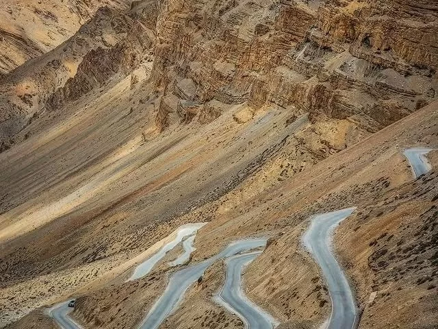 Gata Loops hairpin bends on Manali-Leh highway during golden hour, featuring zigzag roads, rugged brown mountains, perfect thrilling drive Ladakh tour package. 