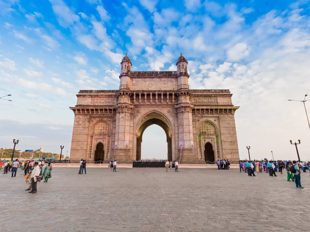 Gateway of India wide-angle day view with tourists exploring the grand Indo-Saracenic arch under a vibrant blue sky, showcasing Mumbai’s iconic waterfront monument and popular sightseeing attraction.