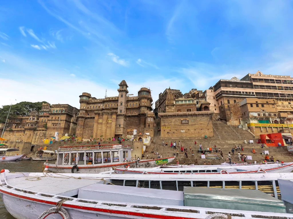 Munshi Ghat palace at Varanasi during clear day, featuring Darbhanga Ghat towers boats crowds, perfect cultural Uttar Pradesh tour package.