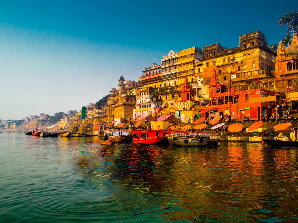 Ganges ghats at Varanasi during golden hour, featuring colorful temples, boats, river reflections, perfect spiritual Uttar Pradesh tour package.