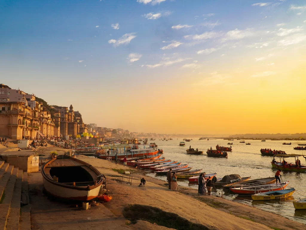 Boats along Ganges River at Varanasi during sunset, featuring ghats crowds reflections, perfect adventure Uttar Pradesh tour package.