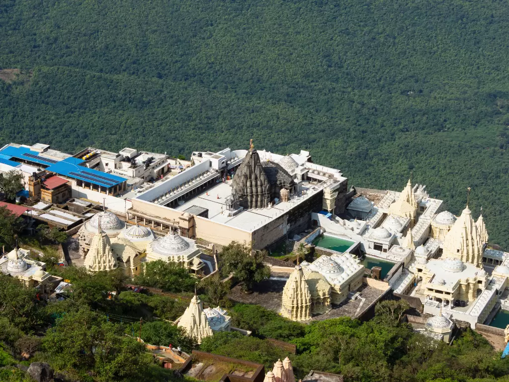 Girnar Jain temples at Junagadh during clear day, featuring shikhara, domes, temple complex amid green hills, perfect pilgrimage experience with Gujarat tour packages.