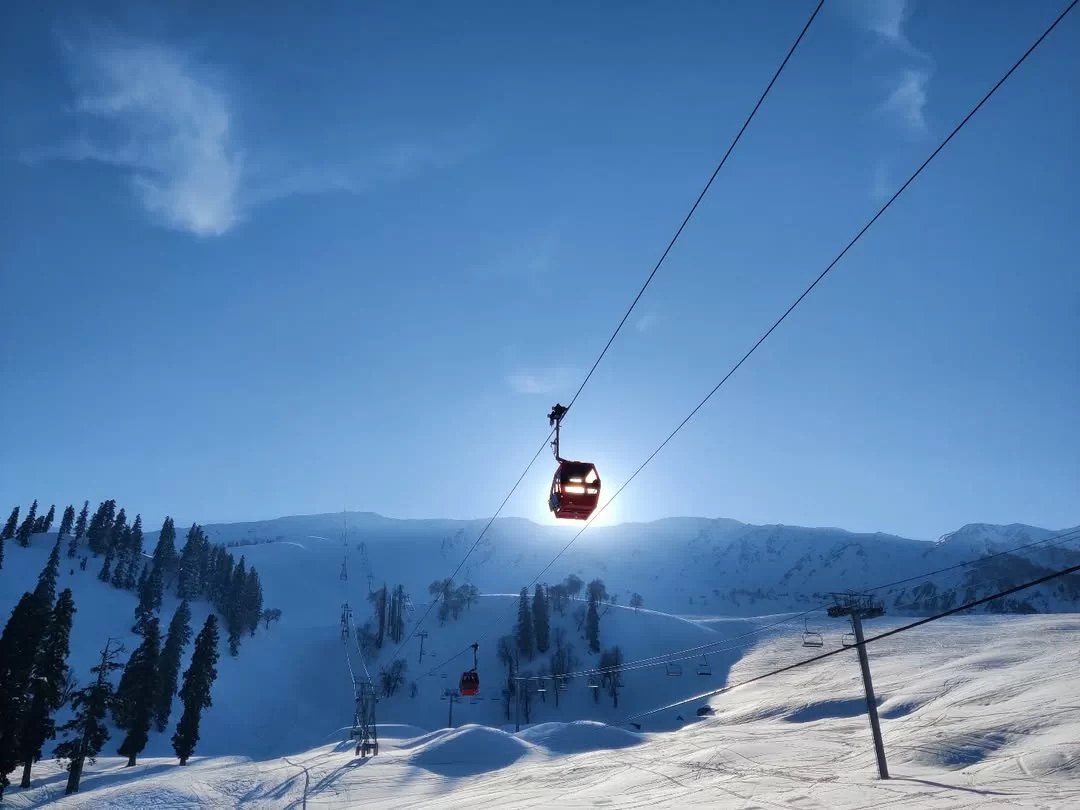 Gondola Ride cable car suspended over snowy mountain landscape with ski slopes and pine trees under clear blue sky.