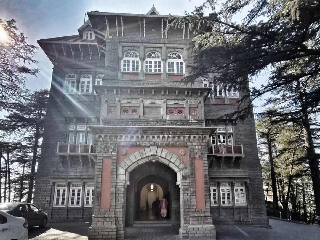 Gorton Castle in Shimla, Himachal Pradesh, a historic grey-stone colonial building with arched entrance, wooden balconies, and tall deodar trees, a heritage landmark featured in Himachal Pradesh tour packages.