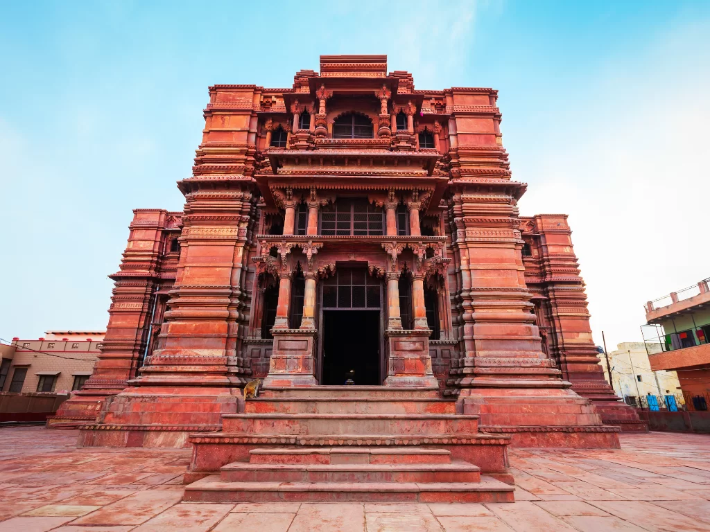 Govind Dev Ji Temple facade at Jaipur during clear daytime, featuring red sandstone architecture, intricate carvings, arched entrance, perfect spiritual experience with Rajasthan Jaipur tour package.