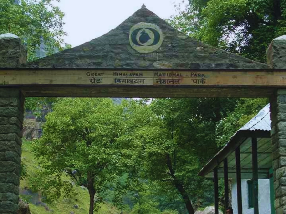 Entrance gate of Great Himalayan National Park featuring a stone arch with park signage, surrounded by lush green trees and forested hills in the Himalayas.
