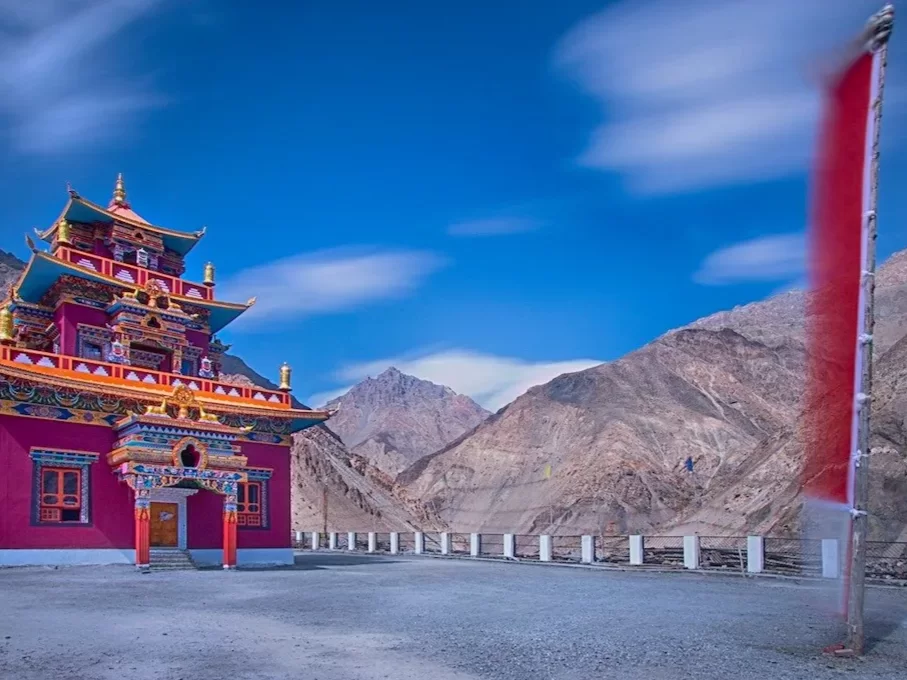Gue Monastery near Kaza Spiti during partly cloudy skies, featuring colorful multi-tiered temple prayer flags rocky mountains, perfect cultural experience Himachal tour package.