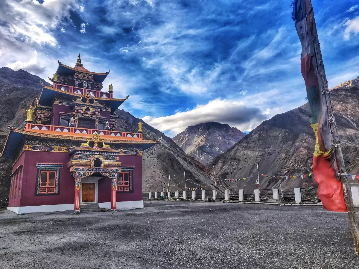 Gue Monastery near Kaza Spiti during partly cloudy skies, featuring multi-tiered maroon gold temple prayer flags rocky mountains, perfect cultural experience Himachal tour package.