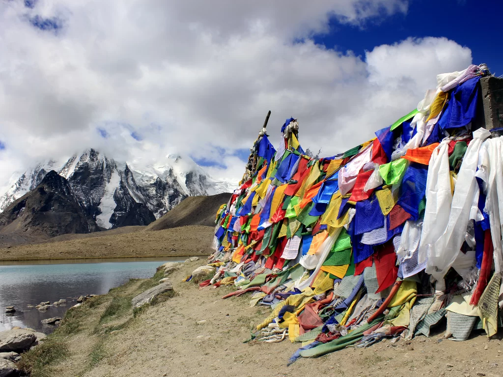 Prayer flags at Gurudongmar Lake North Sikkim during clear skies, featuring snow-capped peaks and turquoise waters, perfect spiritual adventure North Sikkim tour package.