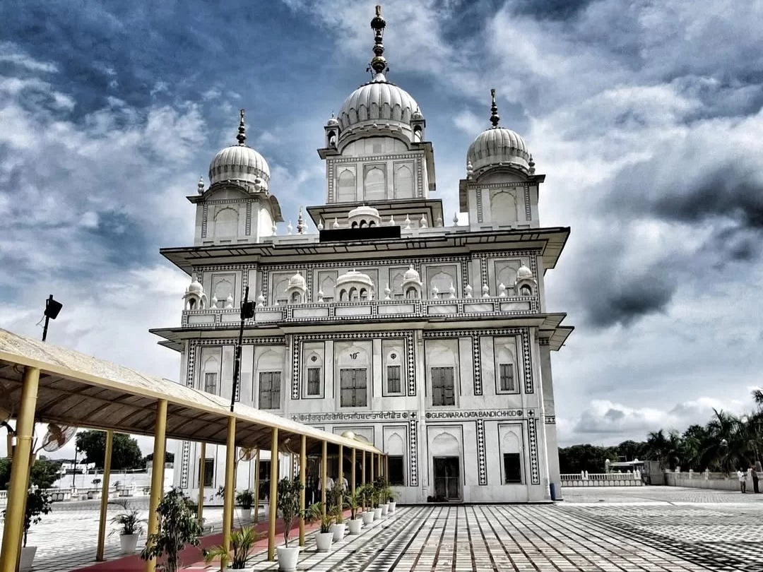 Gurudwara Data Bandi Chhod Sahib in Gwalior featuring white marble domes and a spacious courtyard under dramatic clouds, a revered Sikh pilgrimage site included in Madhya Pradesh tour packages