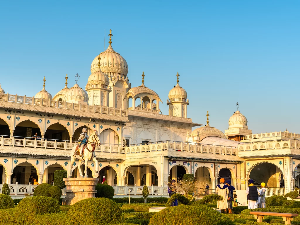 Gurudwara Guru ka Taal at Agra Uttar Pradesh during golden hour, featuring white marble domes, horseman statue, arches, gardens, hedges, perfect spiritual experience Agra tour package. 