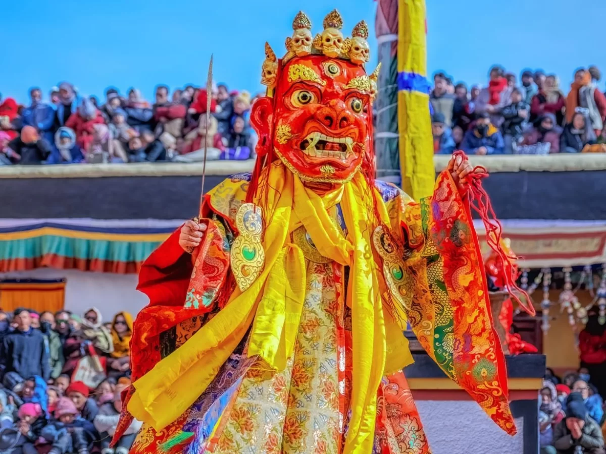 Terrifying red-faced Cham dancer at Gustor Festival Spituk Monastery in Ladakh during sunny festival, featuring ornate crown sword and crowd, perfect cultural adventure experience with Ladakh tour package. 