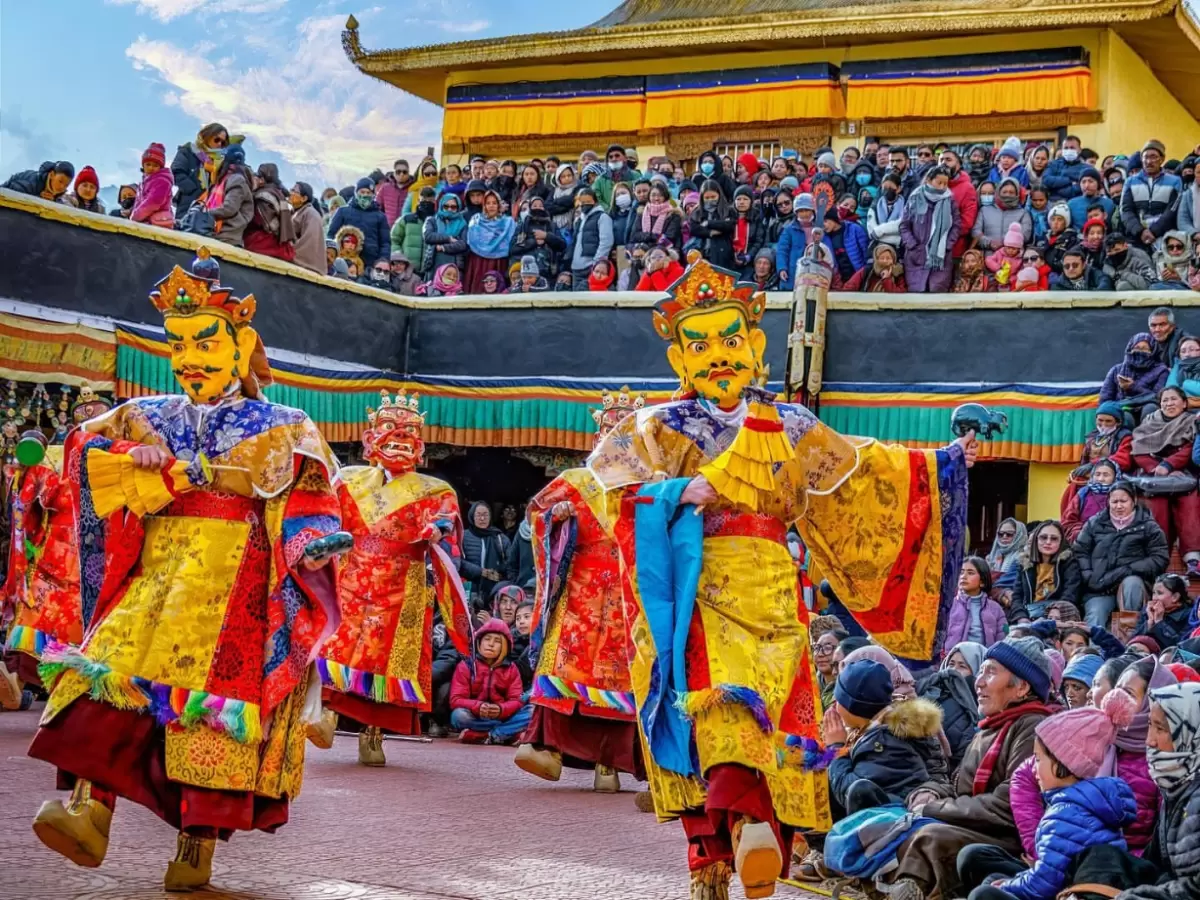 Group Cham dancers in yellow masks at Gustor Festival Spituk Monastery Ladakh during partly cloudy day, featuring golden temple crowd, perfect cultural adventure experience with Ladakh festival tour package. 