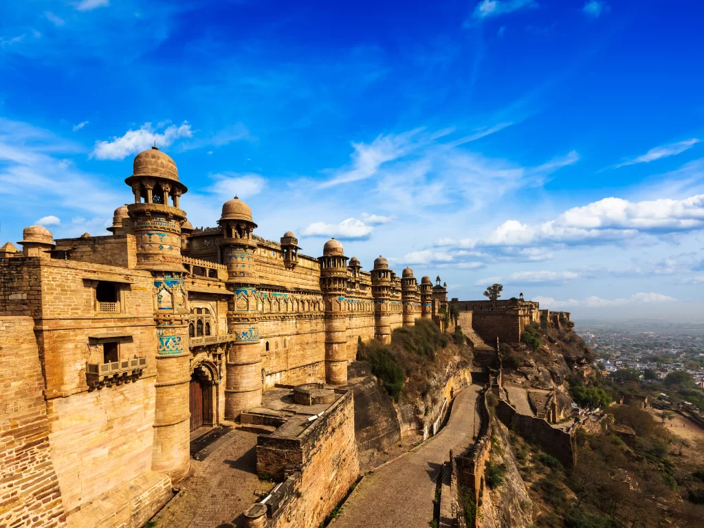 Gwalior Fort Man Mandir Palace during clear afternoon, featuring turquoise tilework domes and ramparts overlooking cityscape, perfect heritage experience in Madhya Pradesh tour package.