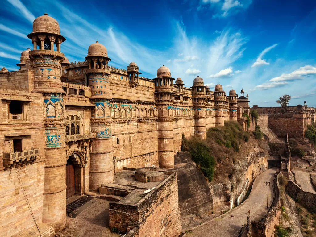 Gwalior Fort during clear afternoon, featuring turquoise-domed bastions and sandstone ramparts on cliff edge, perfect heritage experience in Madhya Pradesh tour package.