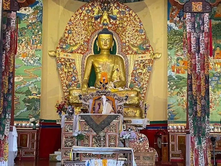 Gyuto Karmapa Temple in Dharamshala featuring grand red staircase, golden rooftop details, and snow-capped Dhauladhar mountains in the background.