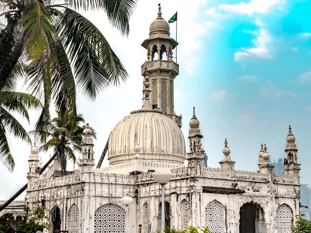 Haji Ali Dargah Mumbai minaret with Pakistan flag against blue sky amid palm trees, perfect Mumbai spiritual heritage tour package.