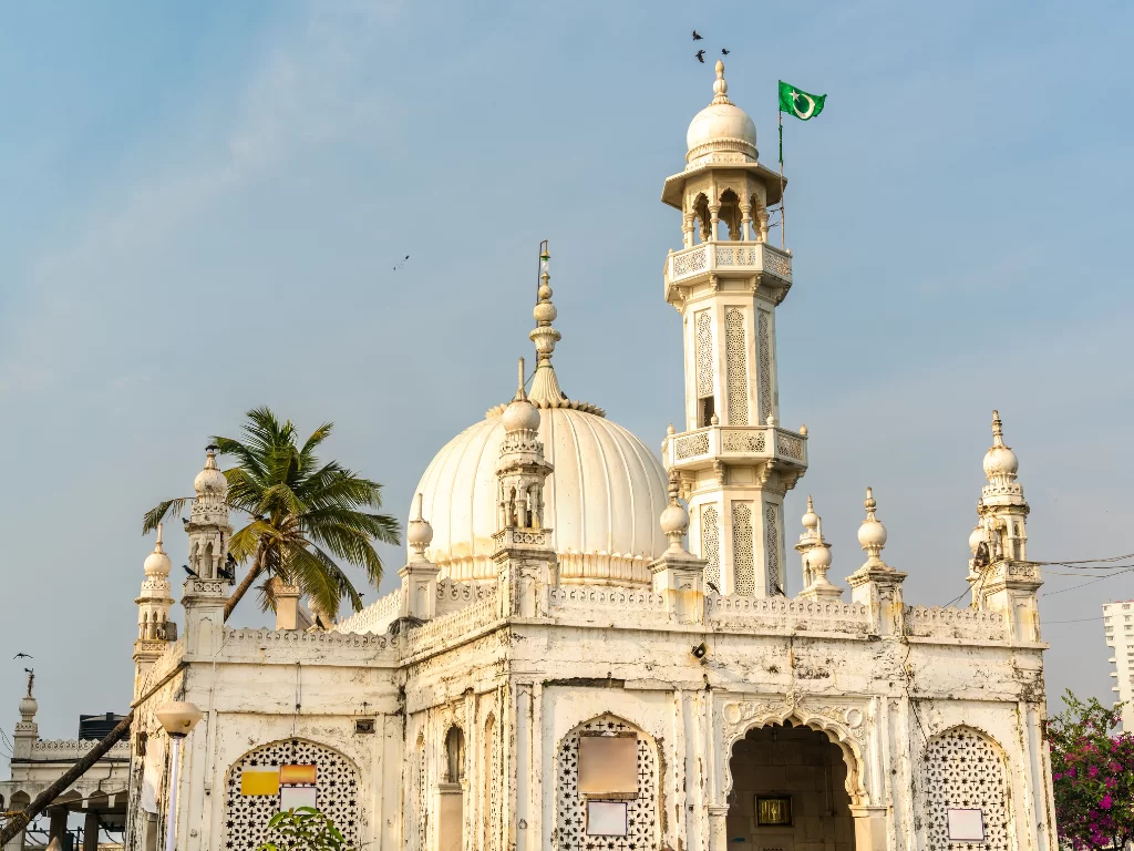 Haji Ali Dargah Mumbai wide angle view with Pakistan flag on minaret amid palm trees blue sky, perfect Mumbai spiritual heritage tour package