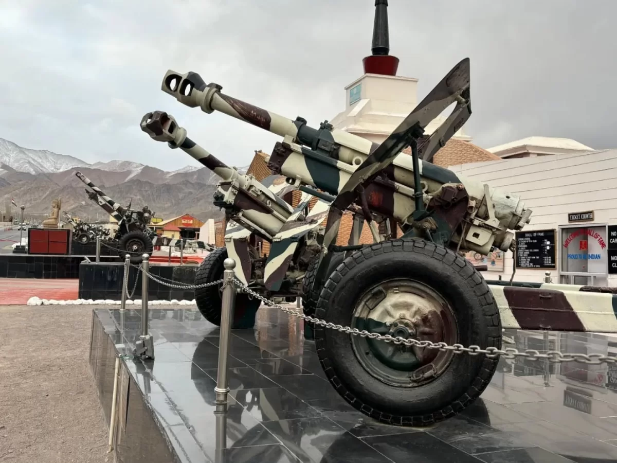 Hall of Fame Leh Ladakh outdoor captured Pakistani artillery twin barrel gun camouflage wheels tires chained pedestal white stupa building mountains cloudy sky military war trophy display.