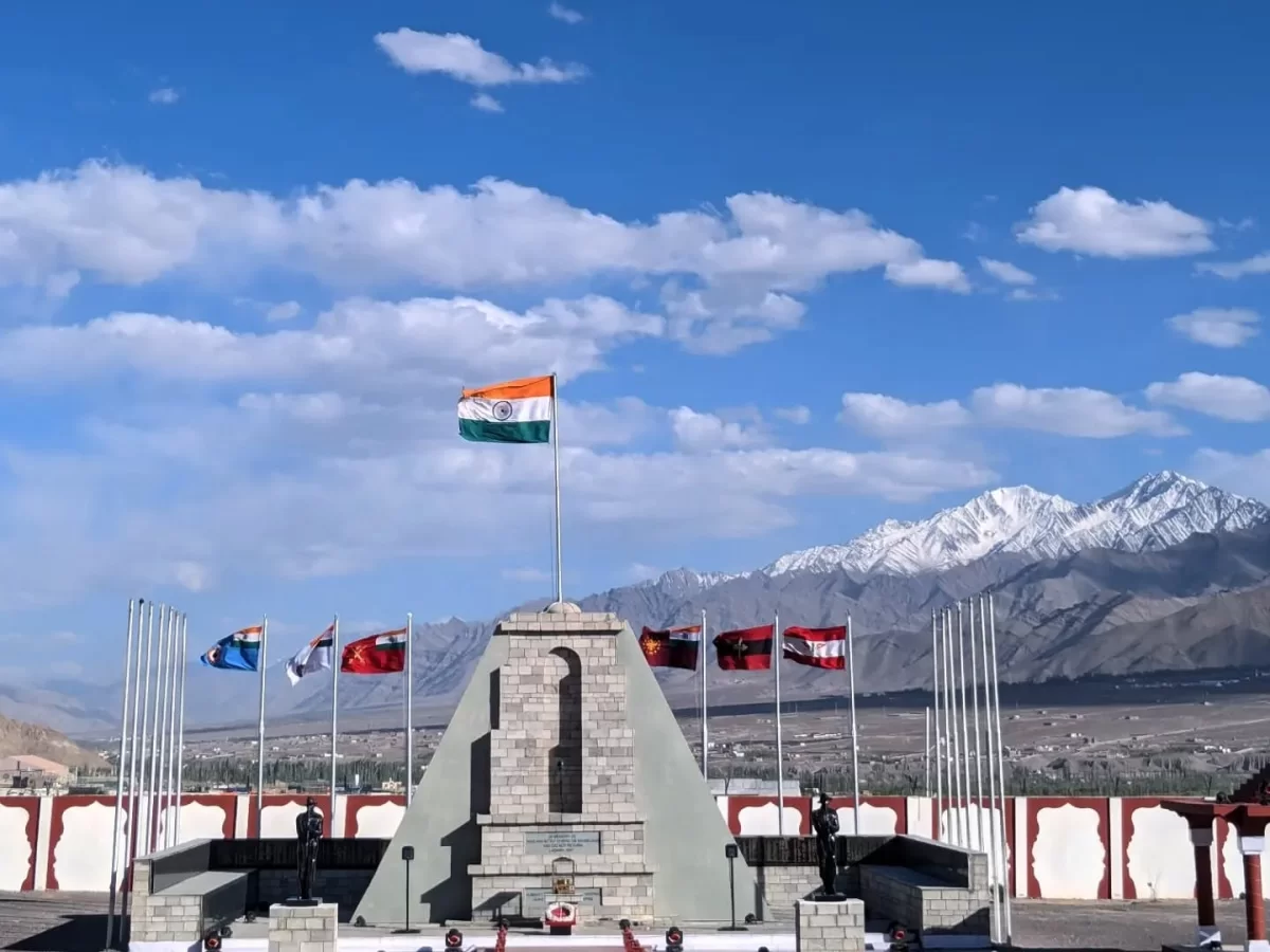 Hall of Fame Leh Ladakh Memorial Hall exterior flags India Nepal UK Turkey others stone pyramid pedestal red white walls snowy mountains blue sky parade ground war heroes monument.