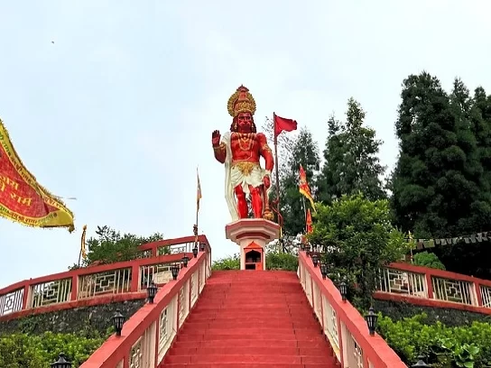Large Hanuman Temple statue atop red stairway in Kalimpong, West Bengal, surrounded by greenery and temple flags, a prominent spiritual site featured in West Bengal tour packages.