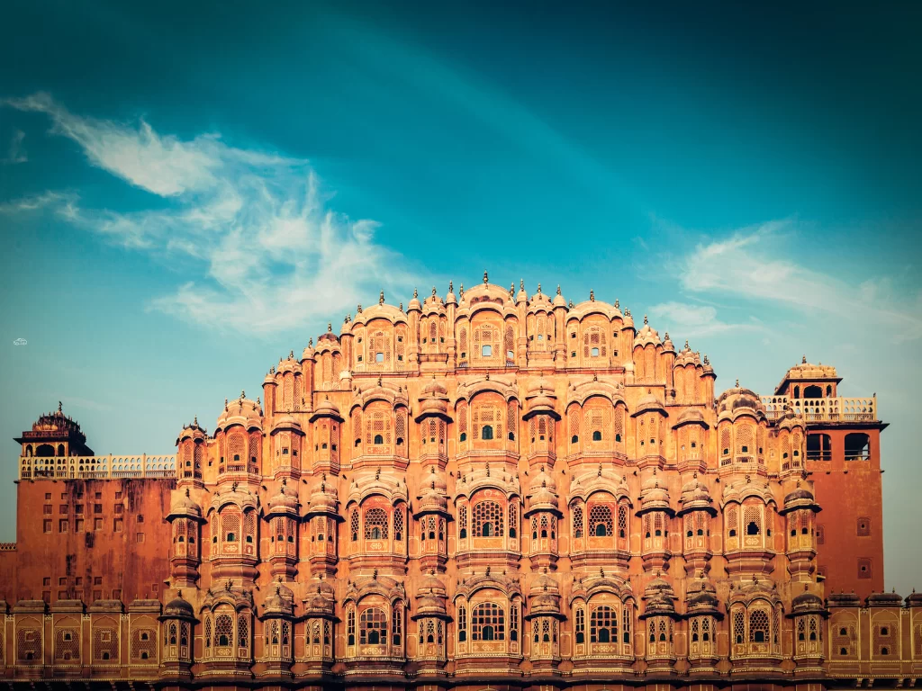 Hawa Mahal front Jaipur golden tones, featuring pink facade jharokhas domes blue sky clouds, perfect romantic experience Rajasthan tour packages.